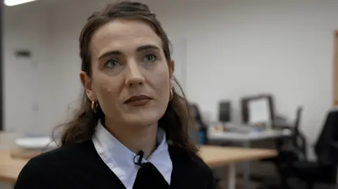 Georgia Poncia/BBC Picture of a woman with brown hair sitting in an office.
