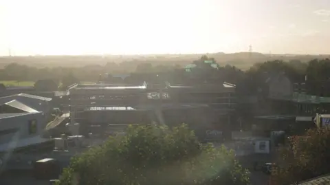 Time-Lapse Systems  A landscape view of the external structure of a cinema with the word 'Gelder' in the corner, next to a Lidl and other buildings with a tree in the foreground.