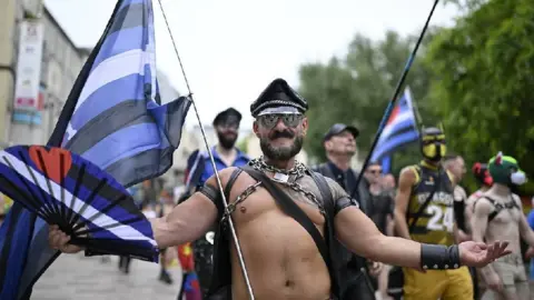 Matthew Horwood/Pride Cymru A man with no top on, wearing a black leather hat and sunglasses looks at the camera with his arms held out by his sides