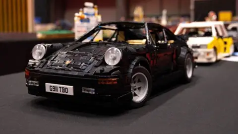 bricktastic A lego build of a black sports car and a white sports car behind it are on a dispaly table.