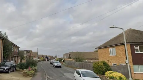 Cerne Road is seen in a Google street view with cars parked along the sides of it. The houses are a mix of bungalows and semi-detached with pitched roofs.