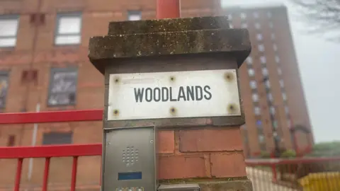 Simon Thake/BBC A metal intercom next to a redbrick tower block entrance