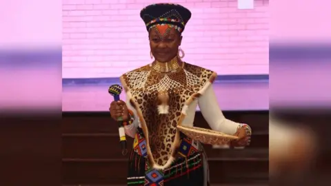 Sarah Sakala is smiling at the camera wearing a native Africa outfit.