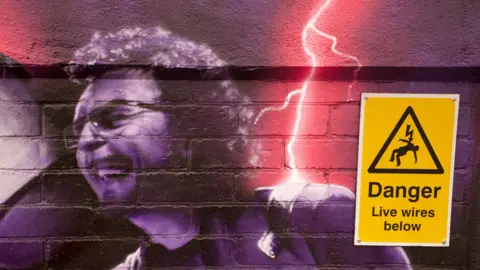 John Bray Spray painted image of band member Tony Iommi being struck by lightning. There is a sign on the mural saying "Danger, live wires below".