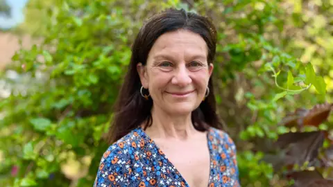 Profile picture of Bridget Smith. She is wearing a v-neck top with a flower pattern. Green foliage is in the background.
