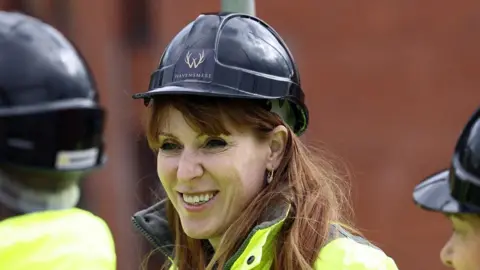 Getty Images Angela Rayner grinning broadly as she wears a black hard hat and yellow high vis jacket