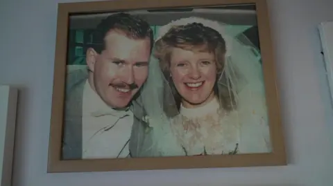 Family handout Barrie and Mo smile for the camera on their wedding day. She is wearing a white wedding dress while he is in a grey suit