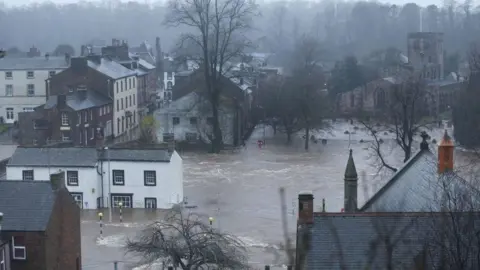 A town with flood water covering many buildings. A churchyard has just the tops of graves visible.  