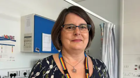 A woman with brown short hair and glasses in a clinical setting.