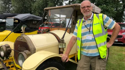 Alan Webber Robert Hadfield in a hi-vis jacket standing by a classic car