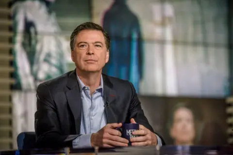 James Comey wears a suit and holds a mug on the set of NBC News' Meet the Press.