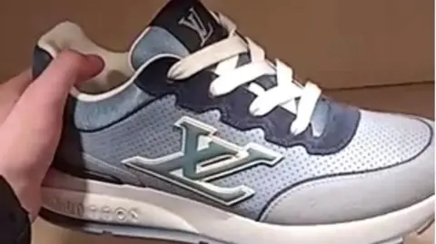 A hand is holding a trainer which is blue and white and has the letters "XL" on one side