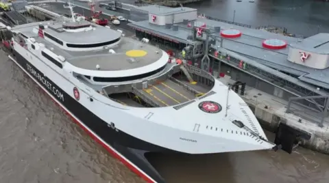 ISLE OF MAN GOVERNMENT The Manannan docked at the new ferry terminal in Liverpool. The vessel is in the Steam Packet colours of white, red and black and it has the logo on the top of it's stern. The three-legs-of-Mann symbol can be seen on the terminal buildings.