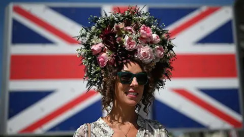 Getty Images A woman wearing an elaborate headdress with roses and other plants on it stood in front on a Union flag.