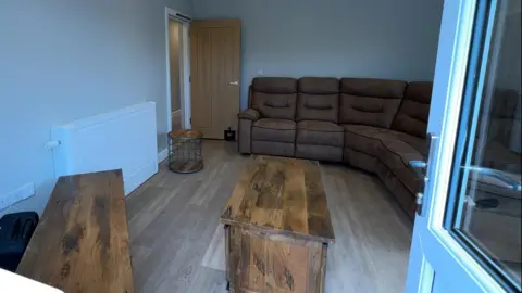 A living room with brown furniture and a wooden floor seen through the doorway from the garden