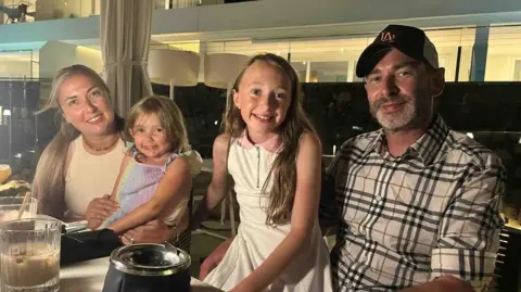 Sarah Rimmer A family of four with two daughters pictured at a table during a meal. All smiling