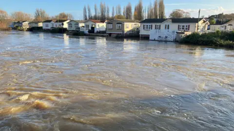 The River Stour at a very high level with a row of mobile homes at the far side of the river