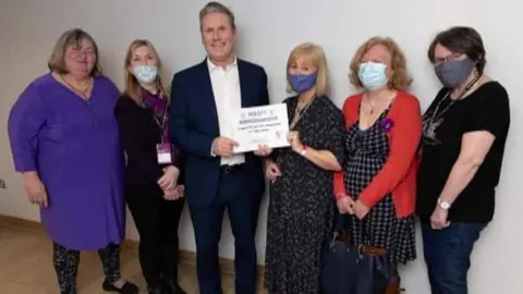 Waspi campaign Sir Keir Starmer holding a white sign, as he stands alongside five women wearing Covid masks - they are all campaigning for compensation for Waspi women