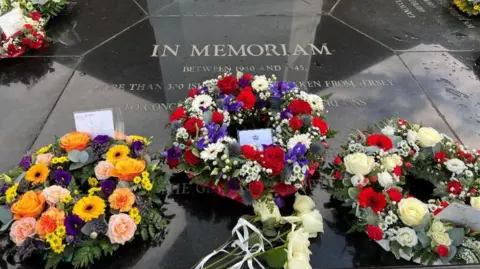 There are three wreaths in front of the memorial to the more than 300 islanders who were taken from Jersey to German concentration camps during World War Two and those who did not return. An engraving in the black stone pays tribute to them.
There is an orange, pink, yellow and purple wreath alongside one with red, white and a blue flowers. The third has white and red blooms and green foliage.
