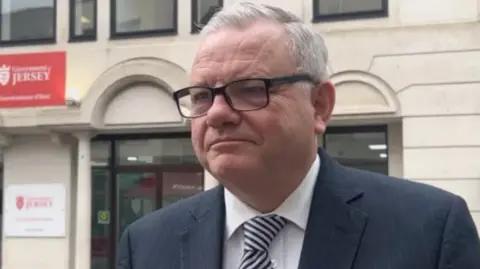Richard Vibert wearing a suit and glasses, standing on Broad street.