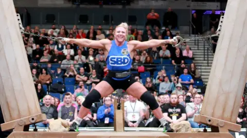 A woman with a blue vest, black short an black knee supports pulls apart two columns