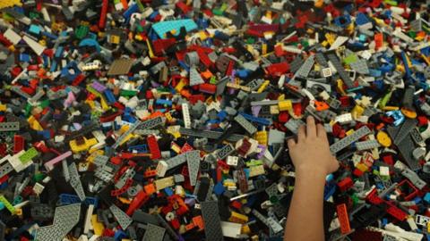A child's hand with hundreds of Lego bricks