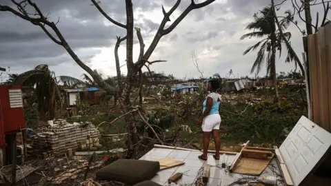 Getty Images A lady stands on the remains of her damaged house in San Isidro, Puerto Rico after Hurricane Maria struck the island.