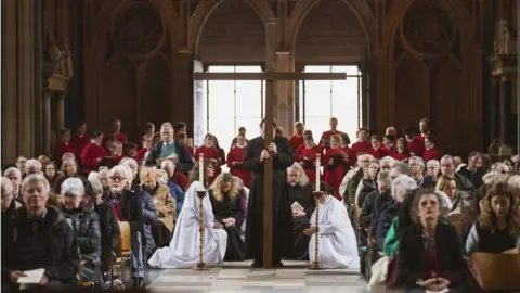 Adam Gasson Worshippers sit in their seats on Good Friday at Bristol Cathedral as a wooden cross is brought in