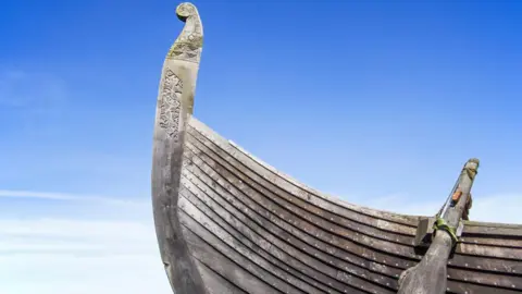 The stern of a full-sized replica of a Viking ship, photographed against a blue sky.