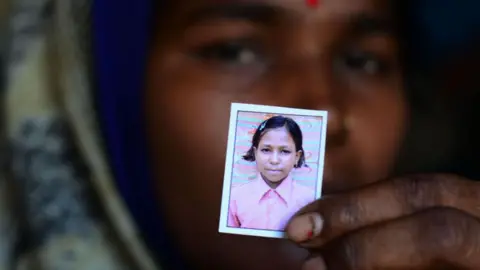 Getty Images Seorang wanita India dalam fokus kabur mengulurkan foto kecil putrinya yang meninggal karena sindrom Guillain Barre selama wabah pada tahun 2019