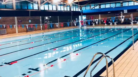 The six-lane swimming pool at the Brentwood Centre. Red, white and blue bunting is suspended over the water.