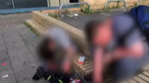Image shows people sitting on a wall with litter around them. Their faces have been blurred. 