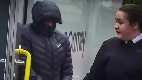 BBC Christopher El Gifari in handcuffs, his face mostly hidden by the hood of a puffy black jacket is let out of a police van