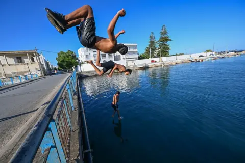FETHI BELAID / AFP / GETTY IMAGES Boys jump and somersault into the water from a road bridge.