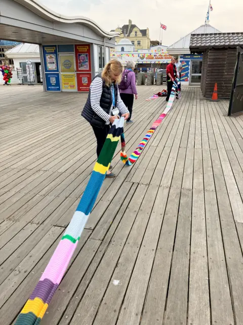 Two people laying the giant scarf down onto the pier
