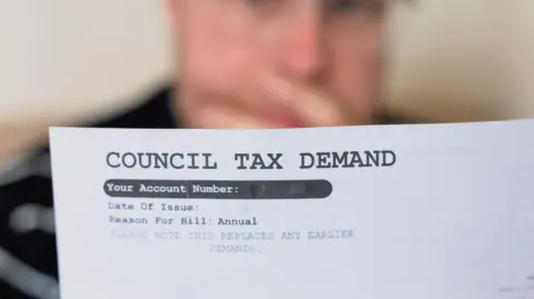 Getty Images A worried looking man, holding his hand over his mouth, is blurred in the background. In the foreground is a white sheet of paper with the words "council tax demand" in large capital letters at the top