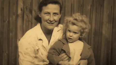 Handout A black and white photo of a woman in a white shirt holding a young girl short curly hair