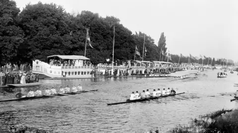 English Heritage/Heritage Images/Getty Images A black and white image of spectators on the college barges and the riverbank watching a boat race during Eights Week in Oxford, around 1860-1922.