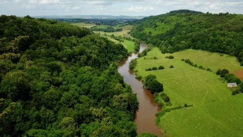 Aerial shot of the River Wye running between hills, forests and green fields