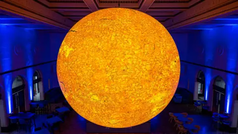 A large bright warm yellow ball which resembles the sun in a blue lit room