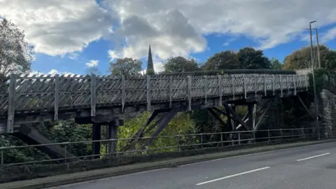 A wooden bridge runs above a road with a church in the background