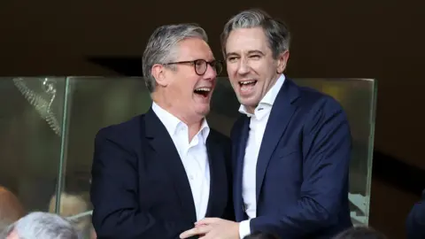 Reuters Sir Keir Starmer and Simon Harris. They are both smiling in celebration. Starmer has grey hair, wearing a dark blazer and white shirt. Harris has grey hair, wearing a navy blazer and white shirt.