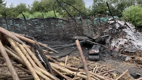 Tom Jackson/BBC The charred remains of a wicker round structure and scorched earth, with trees in the background.