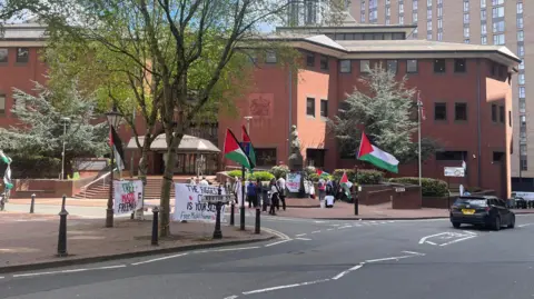 A group of people holding placards and Palestine flags outside a large red brick court building