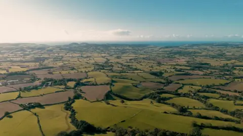 Dorset Council Aerial view of the Dorset landscape with a patchwork of irregular shaped fields and the sea in the distance