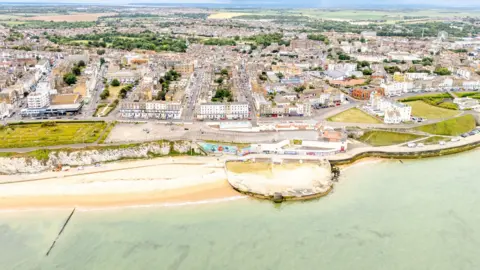 A drone photo of the Cliftonville seafront complex in Margate, Kent. The sea is at the  bottom of the photo, with an aerial shot of a lido above it and housing beyond