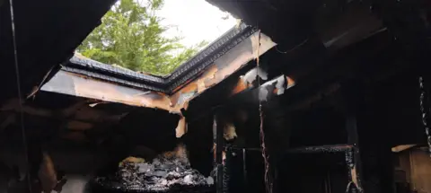 Tom Elliott The ceiling around an open skylight is charred and black. Debris hangs from the ceiling.