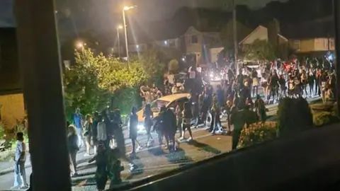 A huge crowd of people seen through a window walking through a residential street. 