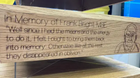 Jon Wright/BBC A close up of the side panel of the wooden candleholder, which includes an outline image of Frank Bright and quote which reads: "In memory of Frank Bright MBE. 'Well since I had the means and the energy to do, I felt I ought to bring them back into memory. Otherwise like all the rest they disappeared in oblivion.'"