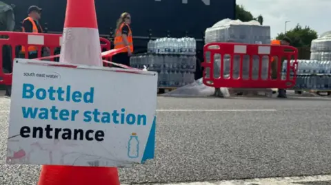 A sign advertising the entrance to a bottled water station near Whitstable, Kent. South East Water workers can be seen in the background of the image.